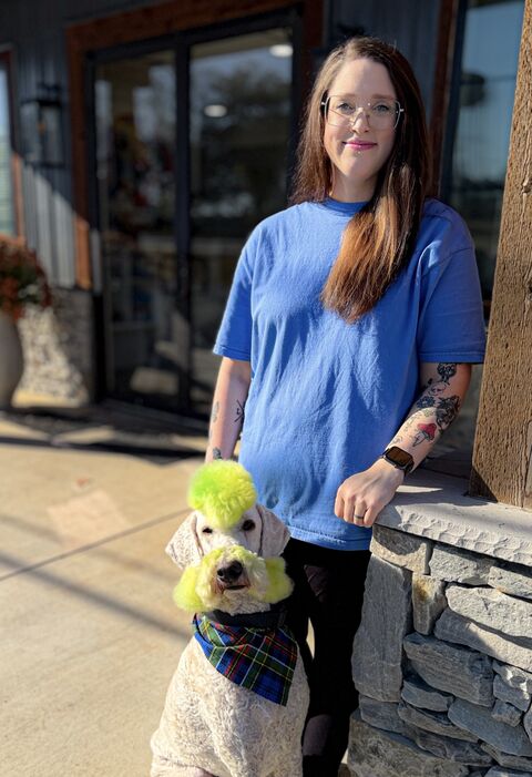 Shelby leaning on a stone wall beside her dog Hudson, whose topknot and face are dyed bright green
